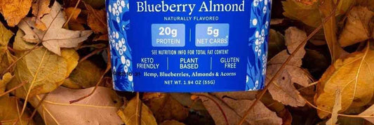 The lower label of a Folk Revival Blueberry Almond cup lying in autumn leaves: 20 g protein, 5 g net carbs, and the ingredient line.